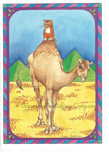 Yellow Tabby young cat sitting atop a camel's hump. The scene is the Egyptian desert with the pyramids in the distance.